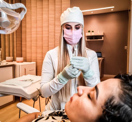 Mulher em uma clínica deitada em uma cadeira recebendo procedimento estético por uma especialista.